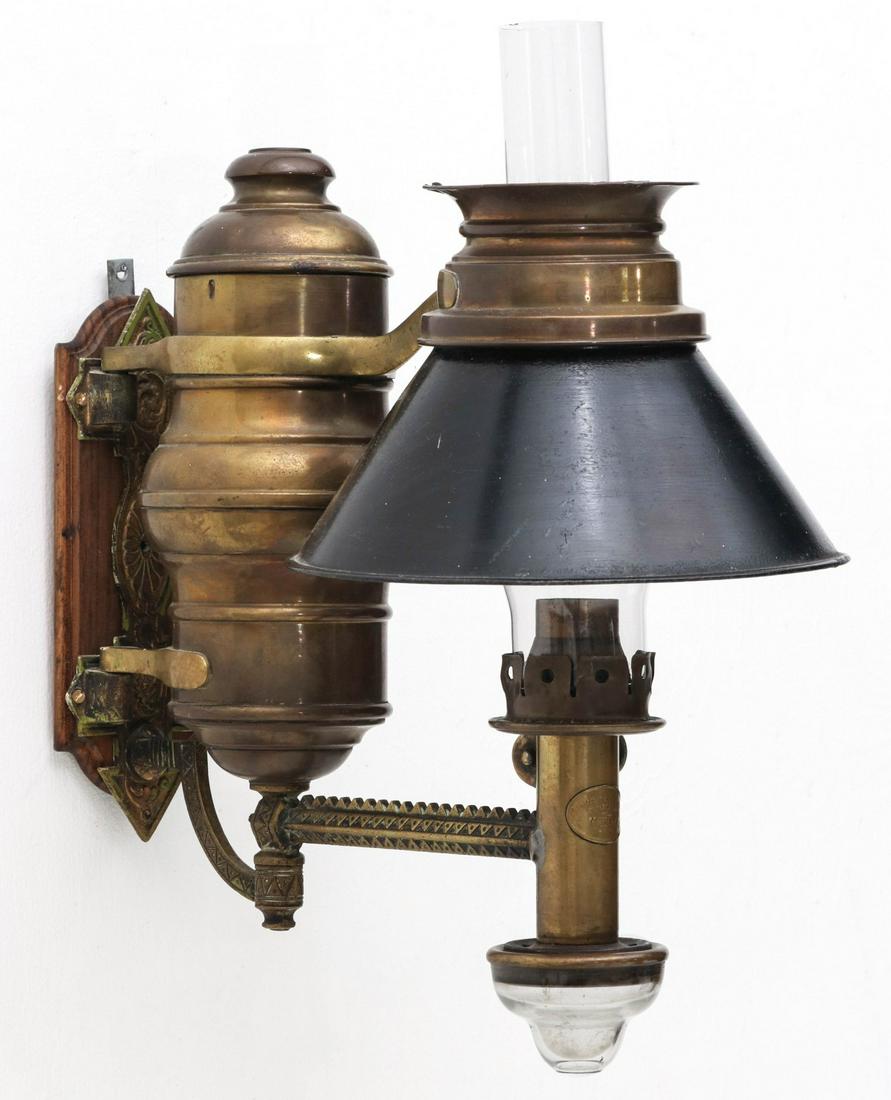 AN ADAMS WESTLAKE WALL MOUNT RAILROAD MAIL CAR LAMP: The ornate cast brass wall mounted fluid lamp bracket with brass fluid reservoir and painted metal shade, clear glass drip cup, embossed oval maker's tag, Acme Mail-Car Side Lamp No. 6, as shown on pa