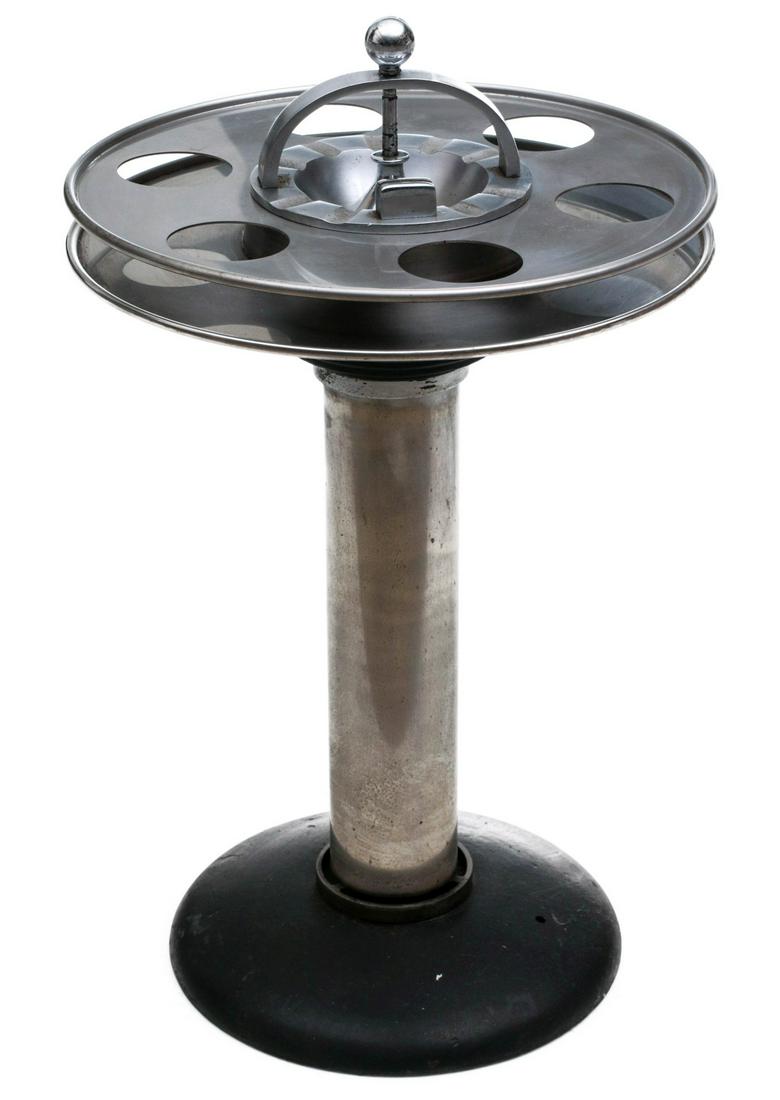 AN ART DECO PERIOD STAINLESS LOUNGE CAR ASH RECEIVER: The two-tier top rings with drink holders, central ash receiver with arched handle, columnar pedestal raised on domed base. Measures 26 x 16 inches. Provenance: The Collection of Ed McHugh, Massillon,