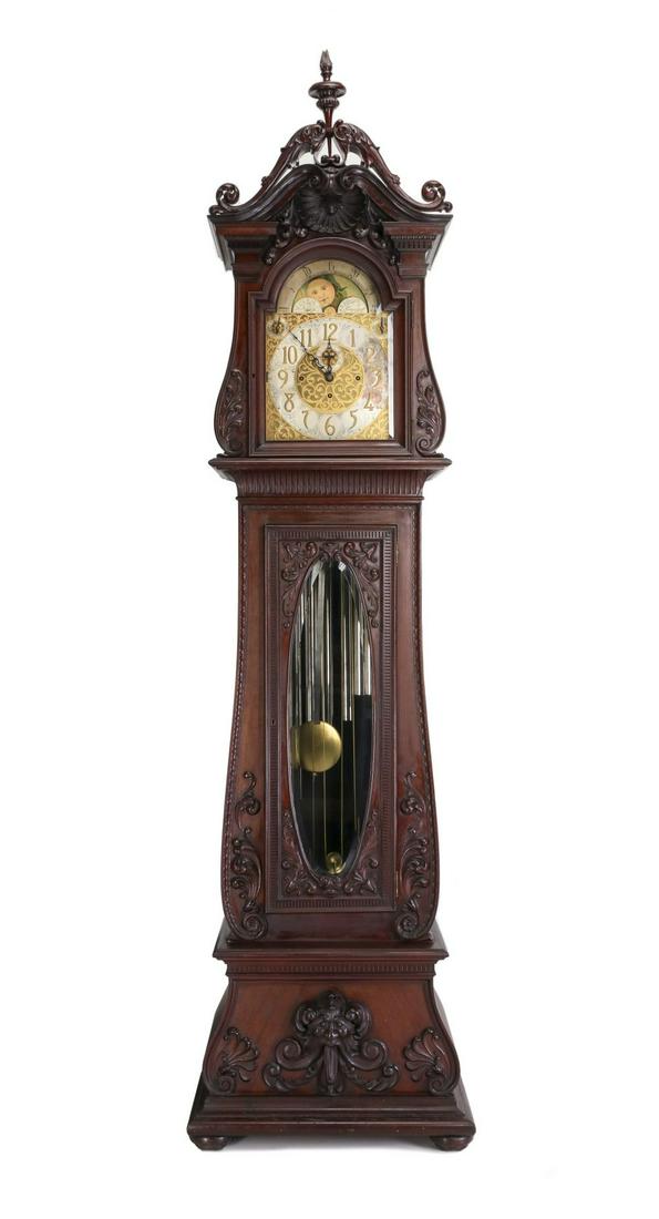 A RARE AND OUTSTANDING HERSCHEDE NINE TUBE TALL CLOCK: The elaborate non-traditional solid mahogany case heavily carved with flame finial between dolphin-like scrolls above a scrolling pediment centered by a deep, dramatic shell carving over the moon phas