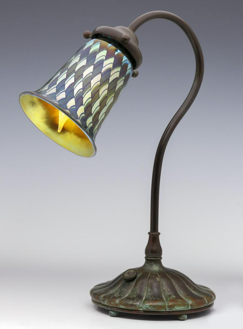 A BRONZE DESK LAMP WITH ORIENT AND FLUME SHADE: The bronze lamp with domed and fluted base issuing a slender arching standard set with art glass shade having fish scale designs and signed Orient and Flume. We happily provide seamless in-house packi