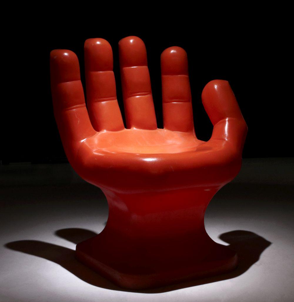 AN ORANGE MOLDED PLASTIC HAND FORM CHAIR CIRCA 1975: The detailed hand and fingers with palm as the seat and raised on a plinth-like base, no markings found. Measures 34.5 x 27 x 26 inches. We happily provide seamless in-house packing and shipping servi