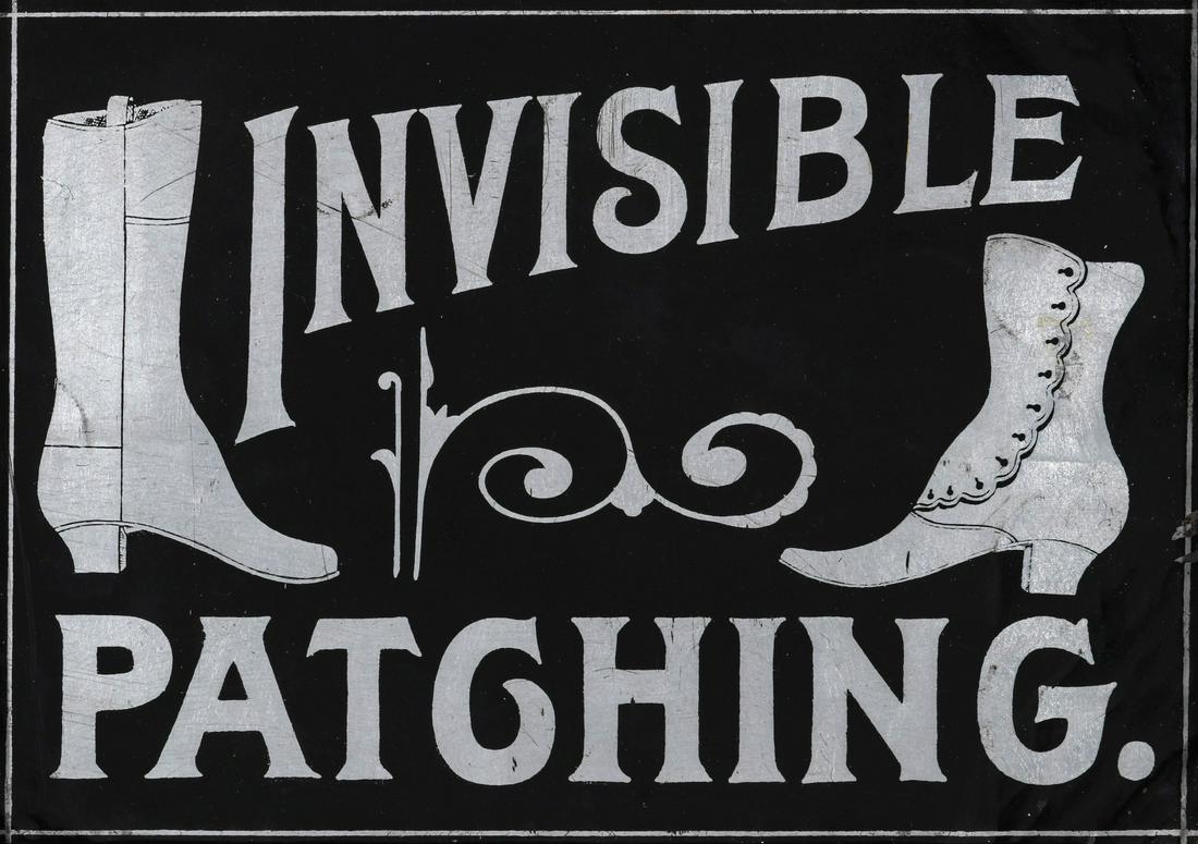 'INVISIBLE PATCHING' TRADE SIGN WITH VICTORIAN HIGH TOP: The tin sign with silver lettering on black ground advertises INVISIBLE PATCHING and pictures a Victorian high top ladies shoe with buttons along with a gentleman's boot. Currently displayed in a cont