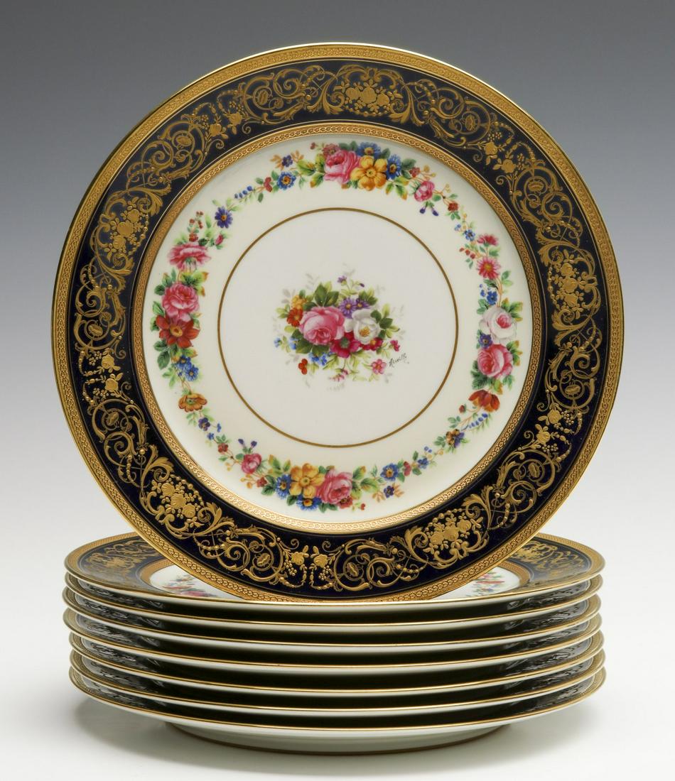 EIGHT AHRENFELDT LIMOGES ARTIST SIGNED SERVICE PLATES: Each with elaborate gold enamels in relief on cobalt border and hand painted garland and floral sprays, artist signed in black, back stamp for C. Ahrenfeldt, retailed by Jaccard's.We happily provide s