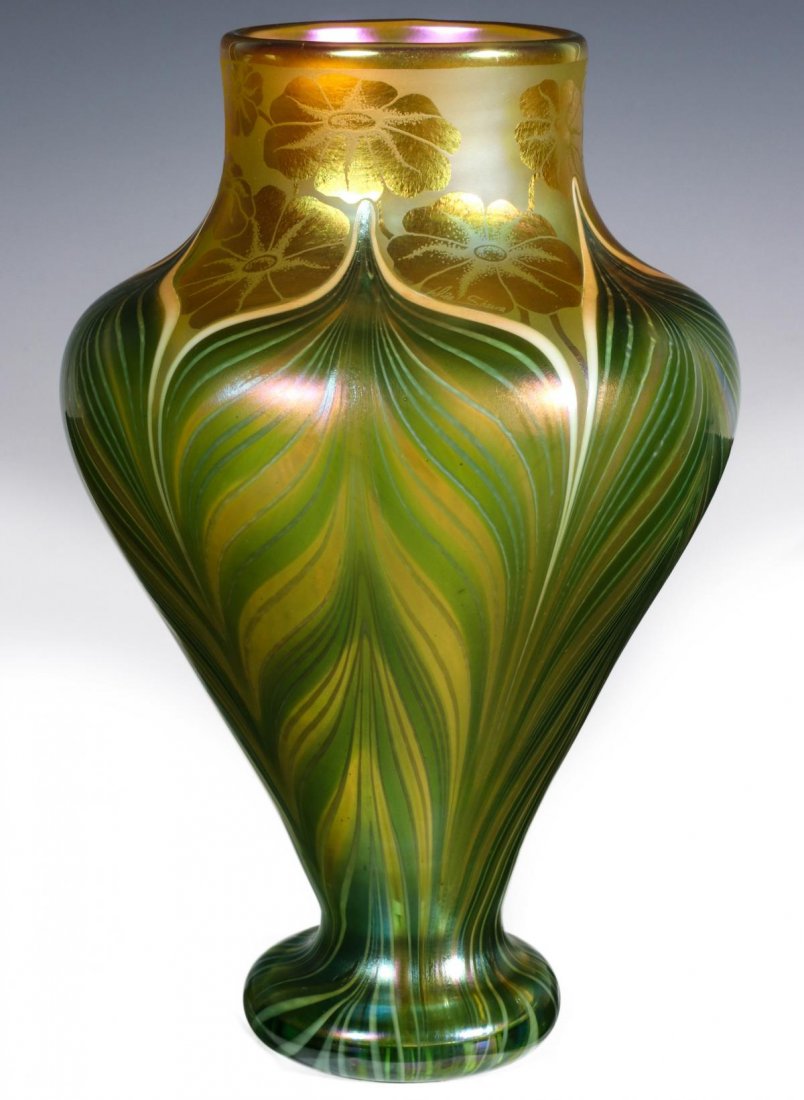 ORIENT AND FLUME ART GLASS VASE WITH PULLED FEATHERS: An amphora form vase with expanded foot, pulled feathers, iridized flowers decorate the top rim, signed with a foil sticker and engraved signature on the base, dated 1982, numbered A21EVs. Measures 8.