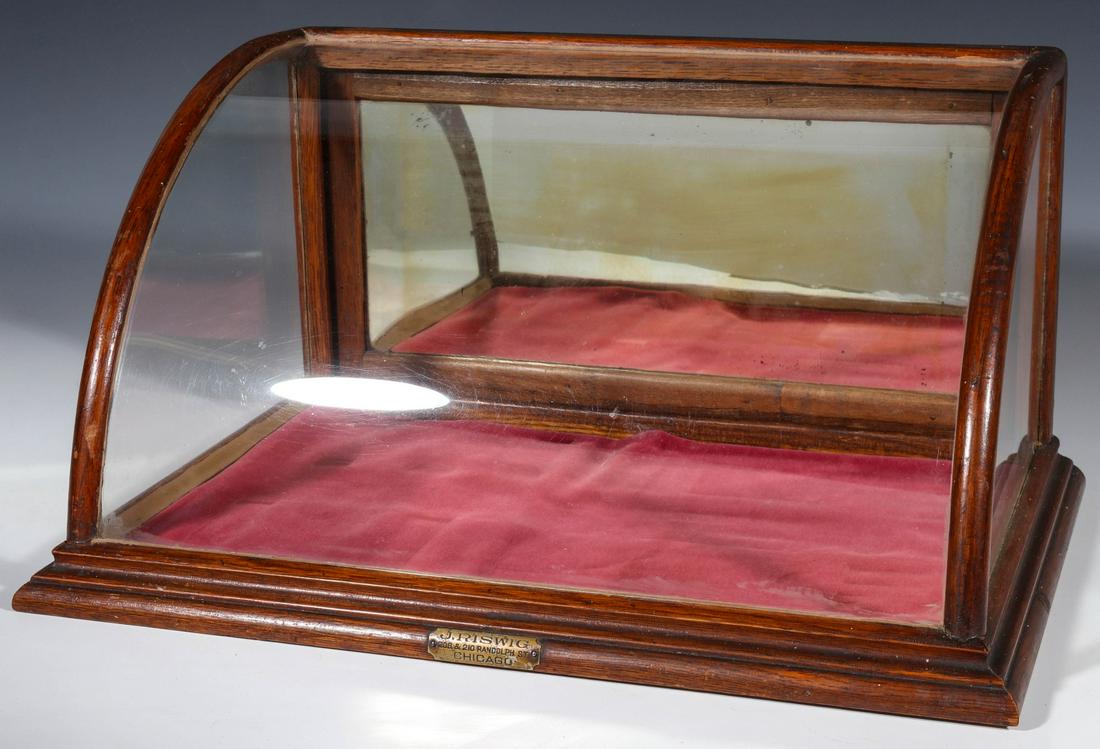 A GOOD SMALL ROUNDED FRONT COUNTER-TOP SHOWCASE C. 1910: The bentwood oak front with bent glass, cove molded base and hinged back door with original mirror, nickel tag for J. RISWIG CHICAGO. Measures 9.25 x 12.25 x 18.25 inches. We happily provide seamless
