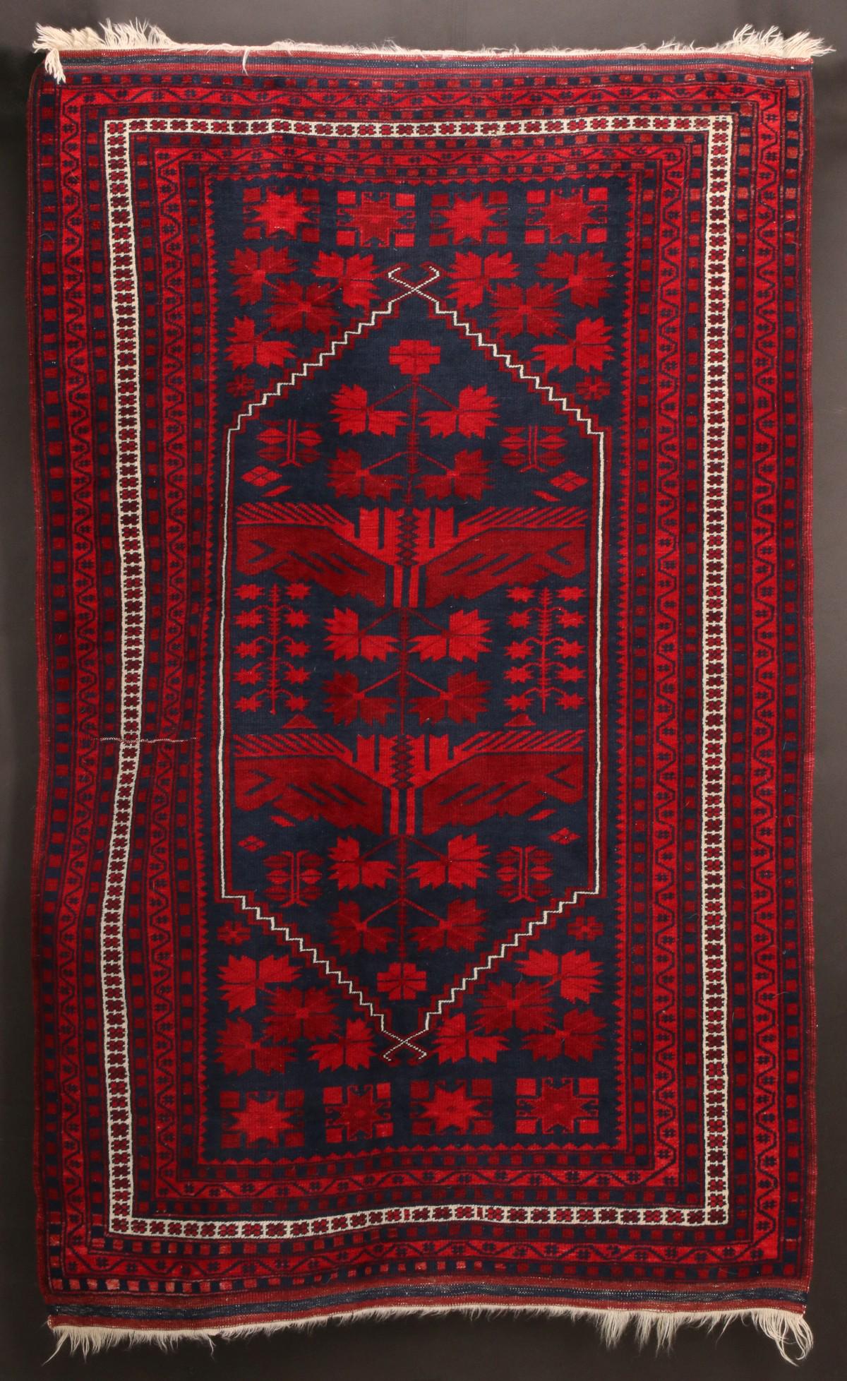 A LATE 20TH CENTURY AFGHAN BALUOCH AREA RUG: The wool weaving with central six-sided medallion on blue ground with red ornaments, four layer edge wrap, flat woven end skirts. Measures 69.5 x 44.5 inches. We happily provide seamless in-house pack