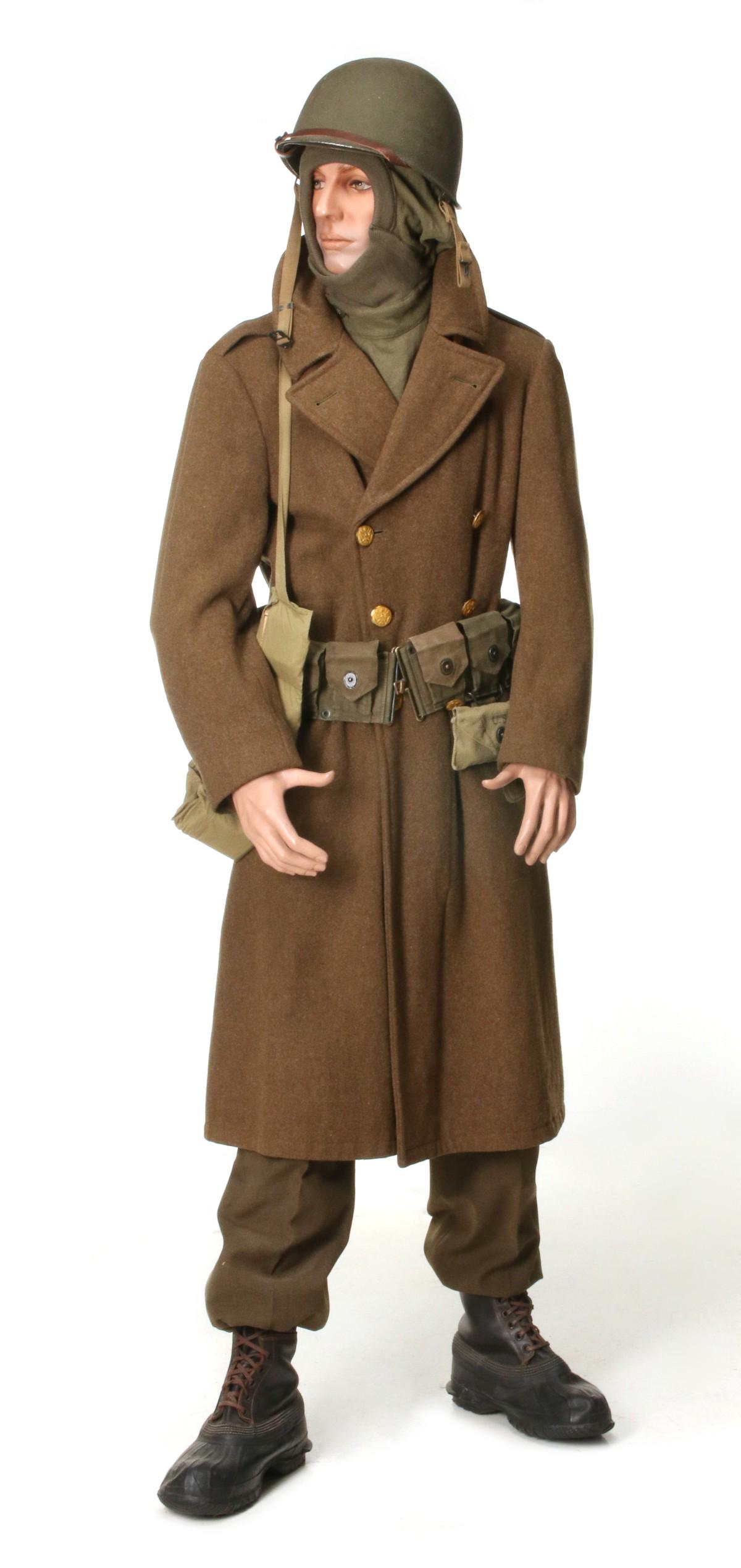 ASSEMBLED OUTFIT HELMET TO BOOTS AS IN BASTOGNE 1944: Wool olive drab shirt, trousers with belt, head and neck wool cover, enlisted overcoat, laced rubber boots, rifle belt with canteen/cup/cover, first aid pouch with bandage, ammo belt, M-1 swivel bail,