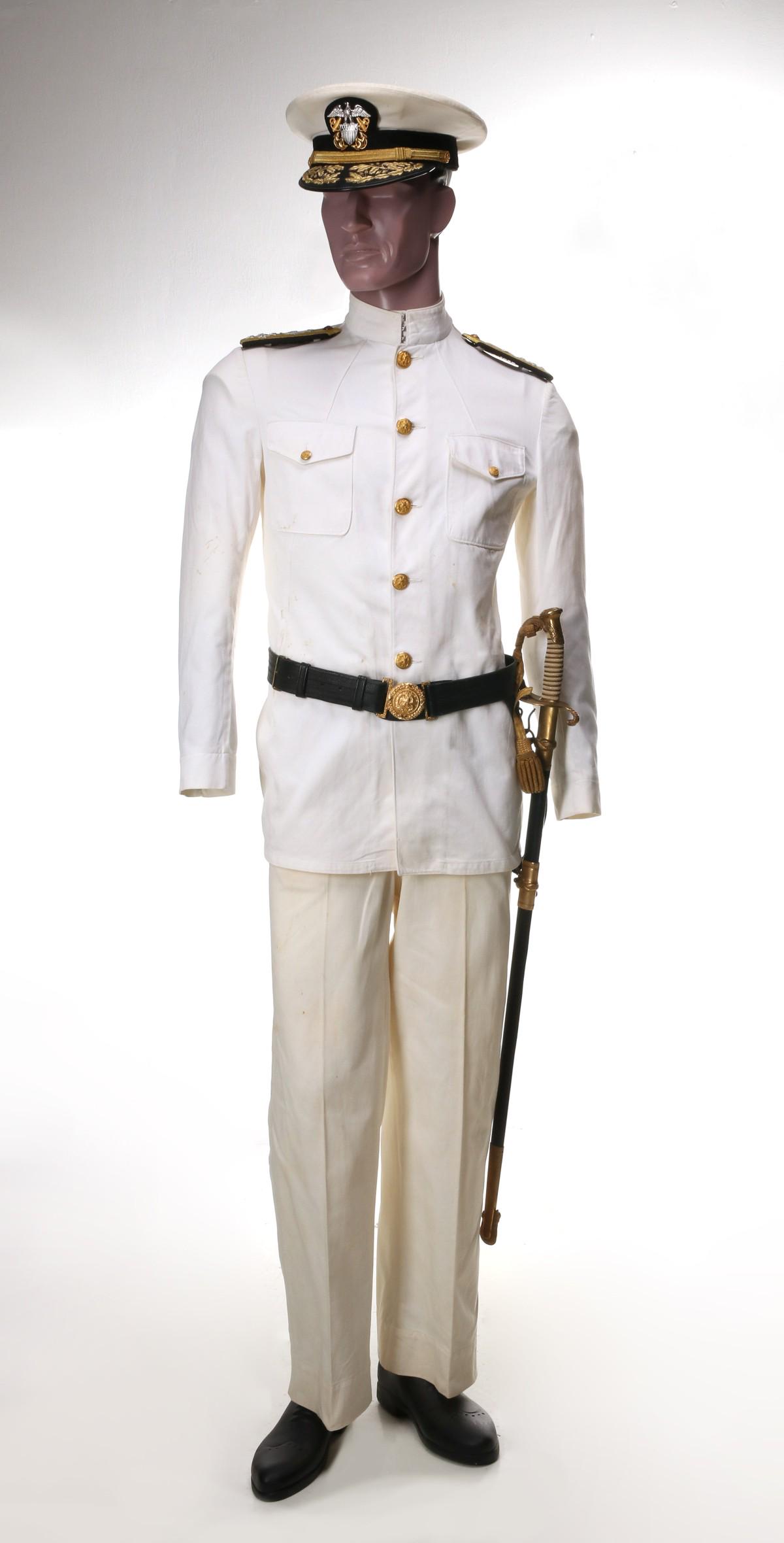 WORLD WAR II ADMIRAL RICHARD GARY COLBERT UNIFORM: White uniform consisting of tunic with shoulder boards, pants, visor cap. NOTE: The leather belt/buckle sword hangers, and sword with name are not original to Colbert, data plaque. Admiral Richard Gar