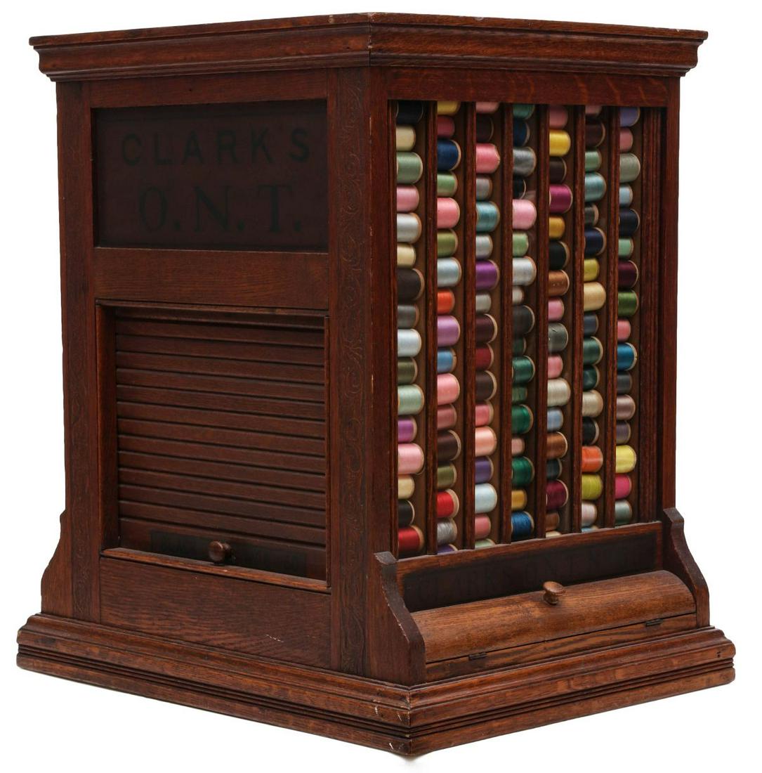 A CLARK'S O.N.T. OAK SPOOL CABINET WITH ROLL FRONT: The top-loading tower form country store merchant's cabinet with two upper hinged top doors and crown molding over two sides with vertical divided glass spool channels over lower door, two sides with