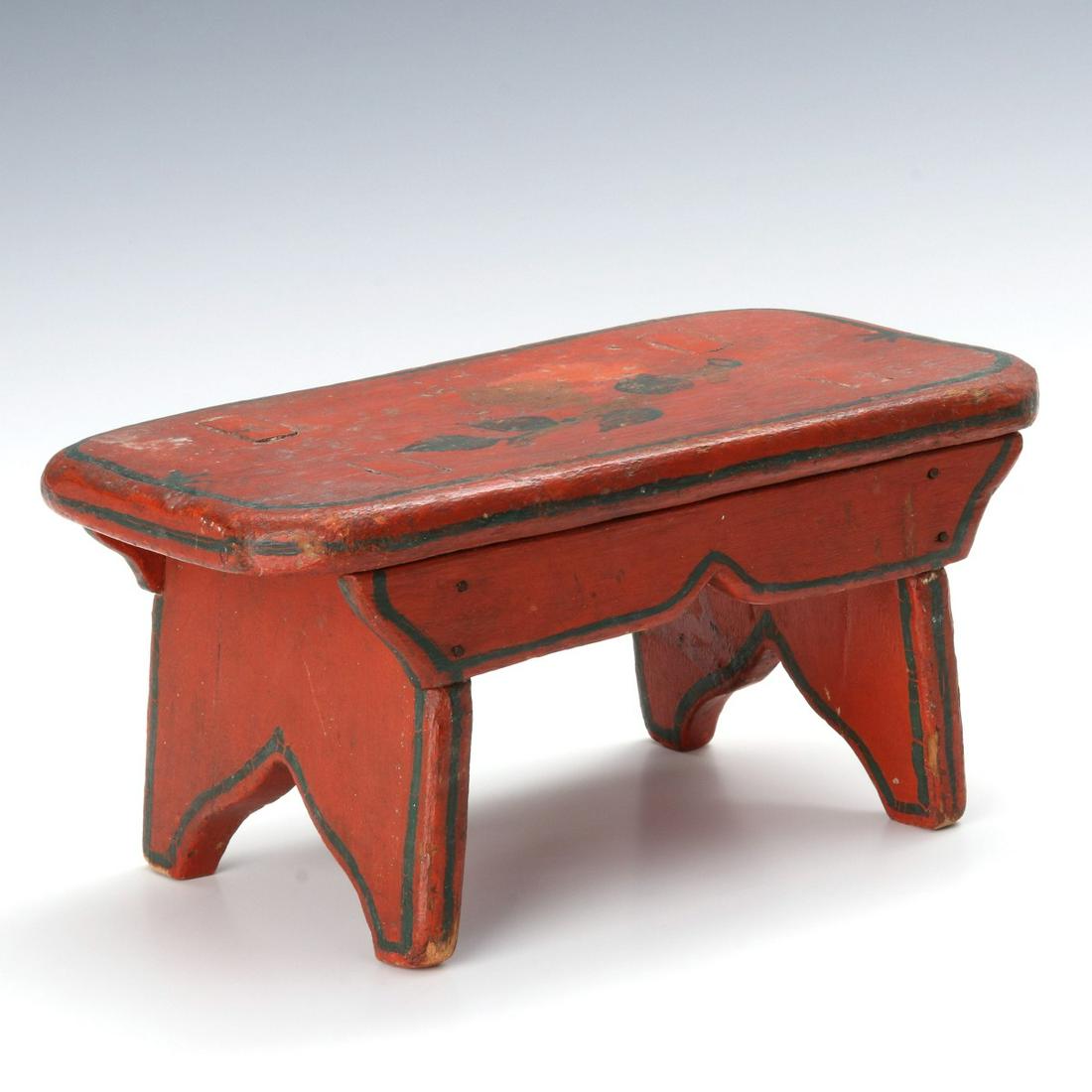 A NICE FOLKY 19TH CENTURY PAINT DECORATED CRICKET STOOL: The overhanging top mortised with each boot jack end spanned by a side skirt and decorated by dark blue paint outline and florals on old red, presumably the original paint in both cases. Measures 5.5