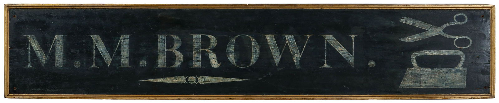 A LARGE 19TH CENTURY TRADE SIGN FOR M.M. BROWN TAILOR: The single pine board with original white lettering and image of tailor's iron with scissors on black ground, gilt molded wood frame. Measures 16.5 x 85.5 x 1.5 inches. Provenance: The Jerry and Cathy