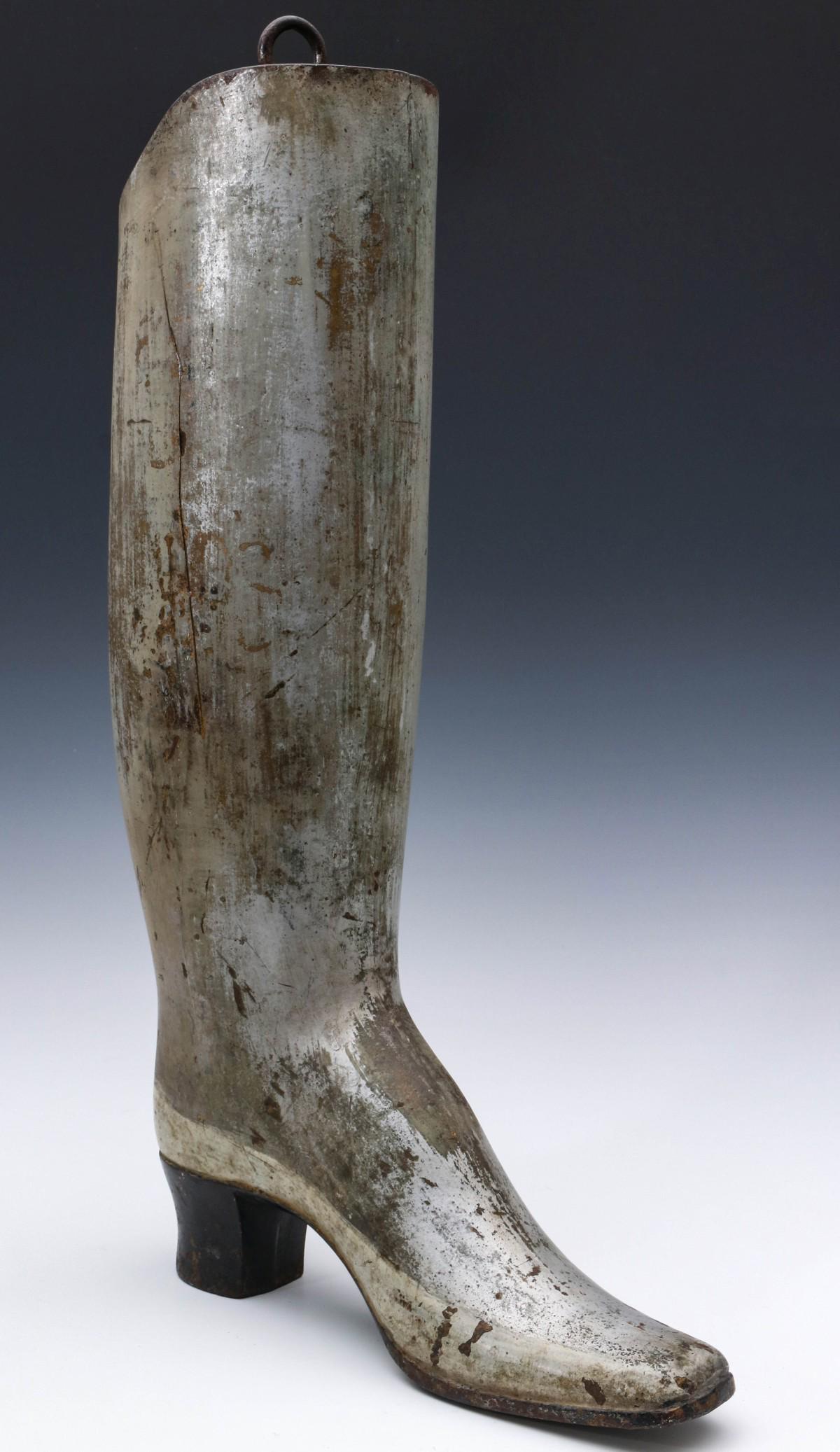 A 19TH CENTURY PAINTED IRON BOOT MAKER'S TRADE SIGN: The hollow iron casting depicts a 19th century dandy's Wellington boot, period silver re-paint over original gilded finish makes for an interesting surface with good patina. Measures 23.5 x 5 x 13 inc