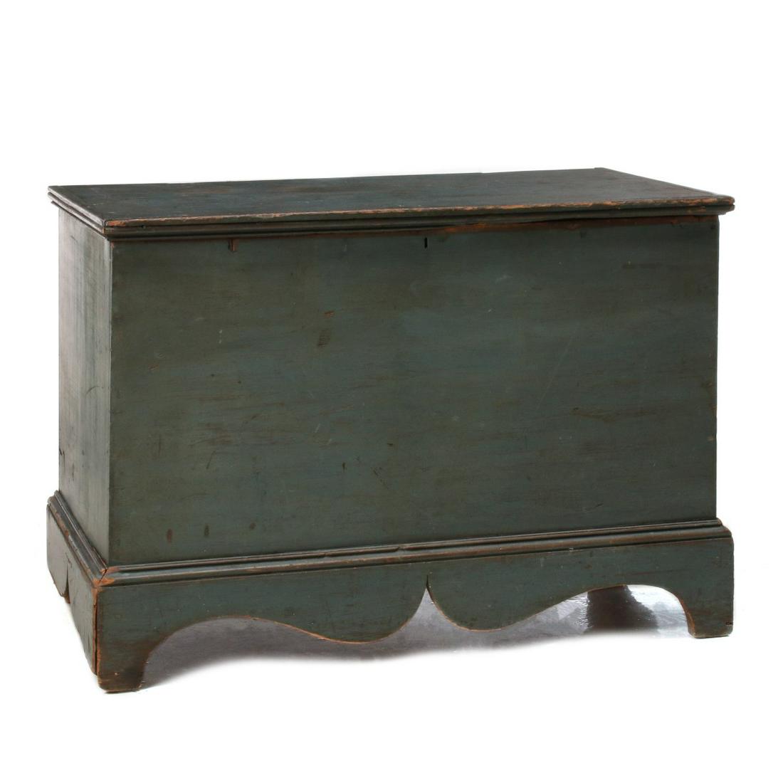 AN EARLY 19TH C. NEW ENGLAND PAINTED BLANKET CHEST: The six board chest with rectangular lid framed in grooved molding over a square-nailed case on base with exuberant scroll-cut skirt and squared corner feet either side of the end cut-outs, iron lock 