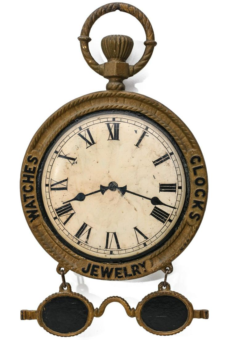 A GOOD WATCHMAKER'S TRADE SIGN WITH FIGURAL SPECTACLES: The two-sided pocket watch trade sign with fancy bail and coined edge iron frame advertising CLOCKS, JEWELRY, WATCHES at 3,6 and 9 cast with tabs for suspending a pair of cast iron eye glasses; the de