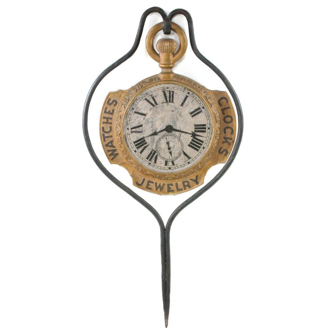 AN UNUSUAL WATCHMAKER TRADE SIGN IN FORGED IRON HANGER: The two-sided model of a pocket watch with ornate zinc bezel and semi-circular tabs touting CLOCKS, WATCHES, JEWELRY in raised letters at 3,6 and 9, zinc insert representing the watch face with hand p