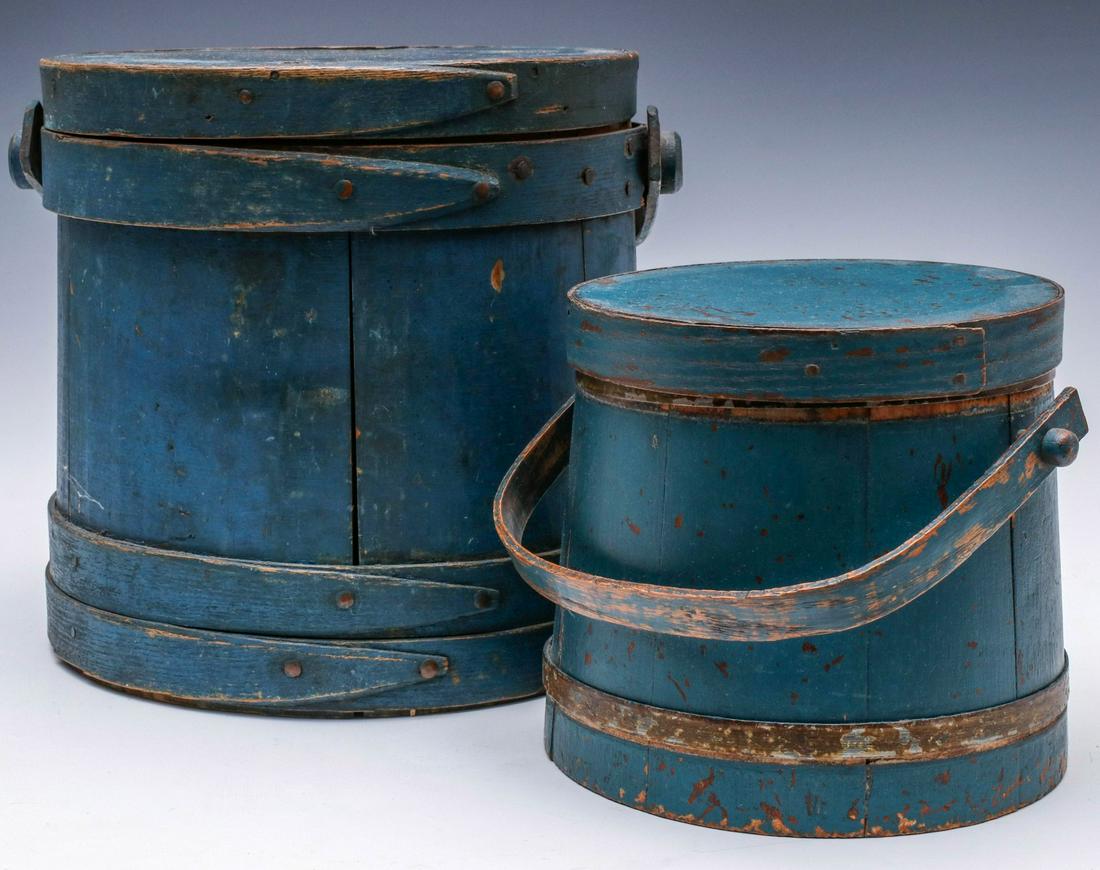 TWO 19TH CENTURY FIRKINS IN OLD BLUE MILK PAINT: The larger with wood staves bound in wood bands with finger laps, bentwood bail handle on wooden peg, old blue paint. The smaller with wood staves bound in two steel bands, bentwood bail handle on woo