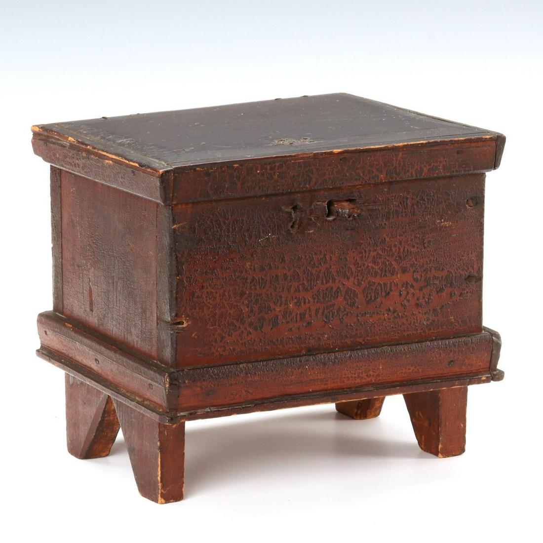 A 19TH C. AMERICAN FOLK ART MINIATURE CHEST IN RED: The folky diminutive six board chest model with framed lid mounted by make-do brass hinges upon case raised on disproportionate boot jack ends, case molding, beveled top - outstanding original surface