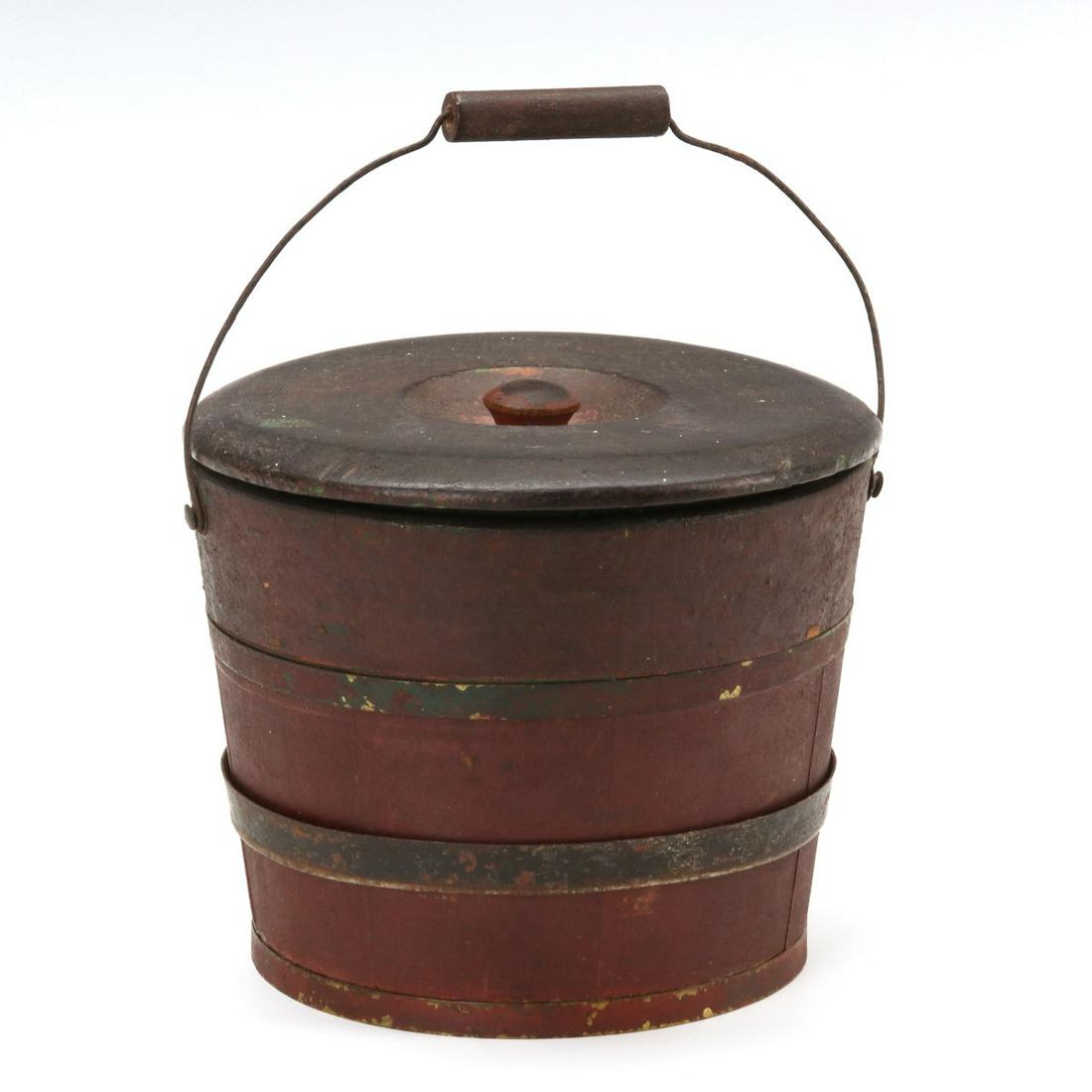 A MINIATURE 19TH CENTURY WOOD STAVE PAIL IN OLD PAINT: The miniature pail or bucket in old red paint and with iron bands, original bail handle with wood, presumably the original turned wood lid shrunken across the grain with age and slightly out of round,