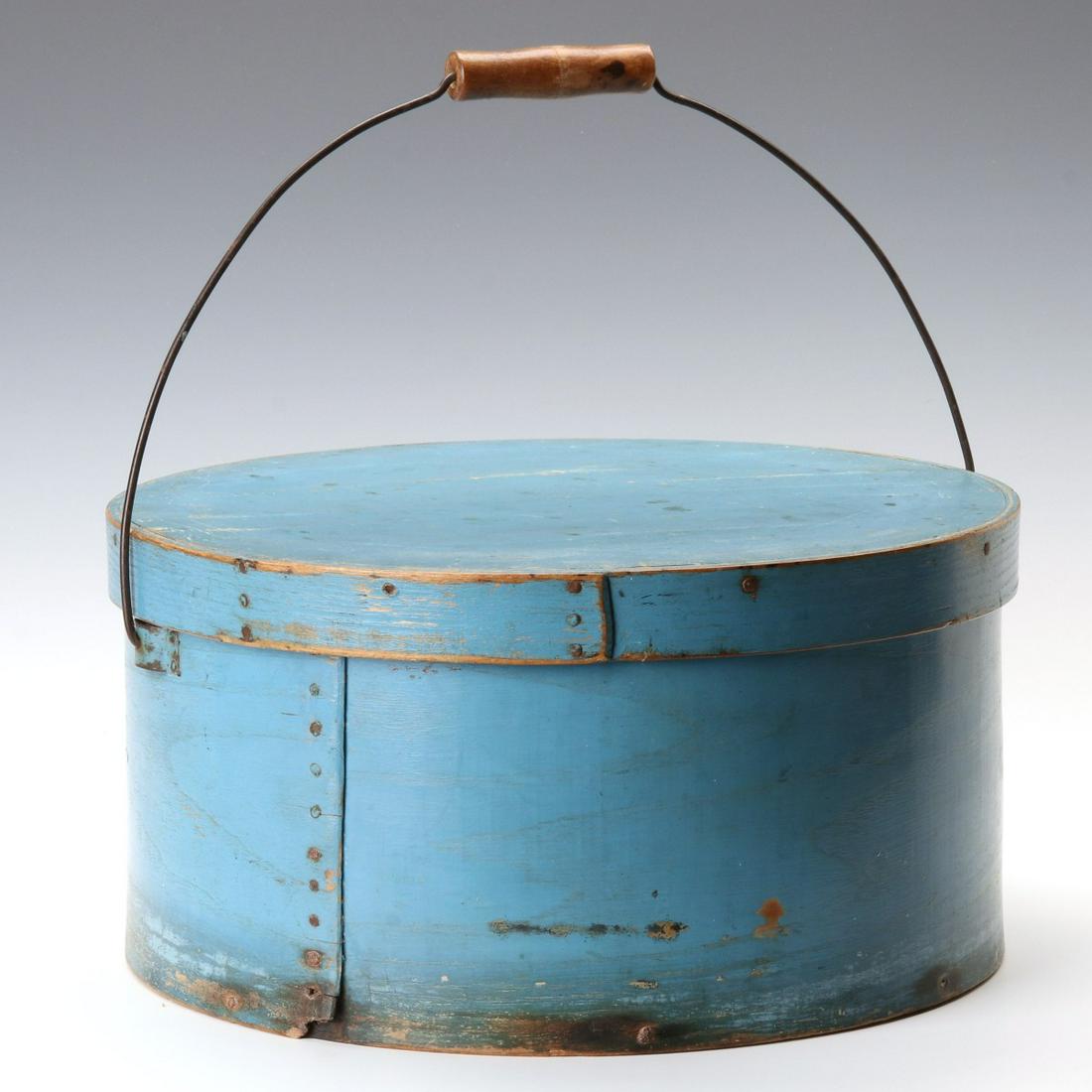 A LARGE CIRCULAR BENTWOOD PANTRY BOX IN OLD BLUE PAINT: The more unusual type with bail handle, the straight seams secured with iron tacks, original blue milk paint, original bail handle assembly with wood roller, nice large size. Measures 7.5 x 15 inches.