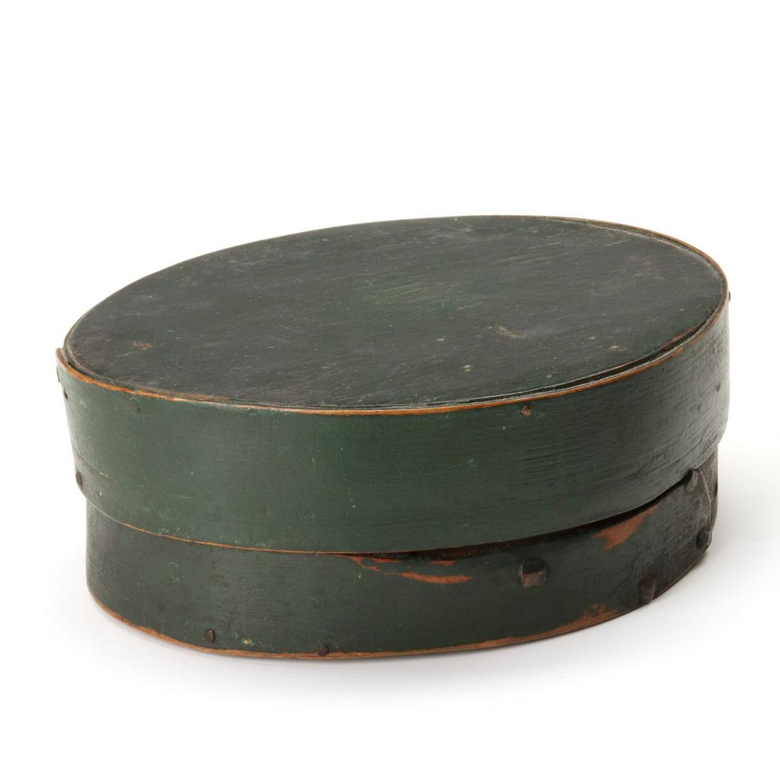 A 19TH C. PRIMITIVE OVAL PANTRY BOX IN OLD GREEN PAINT: The primitive construction and bands secured by rose head iron tacks and nails along with wood peg construction. Measures 2.5 x 7.25 x 6 inches. We happily provide seamless in-house packing and shippi