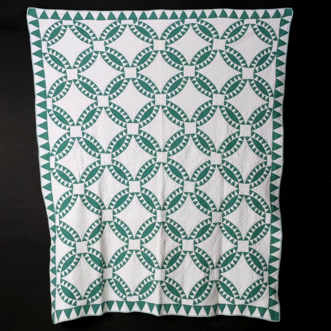 AN EARLY 20TH CENTURY INDIAN WEDDING RING PATTERN QUILT: The green and white Indian Wedding Ring pattern quilt hand pieced and quilted with pieced borders, green binding, white backing. Measures 80 x 64 inches. We happily provide seamless in-house packing a