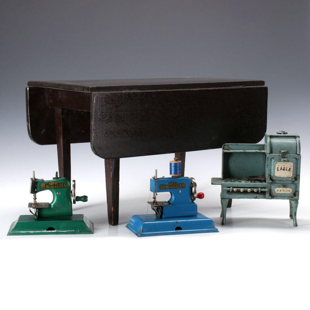 EARLY 20TH C. CHILD'S STOVE, TABLE, SEWING MACHINES: Includes: A doll-sized wood drop leaf table in old brown stain; Two small KAYanEE Sew Master sewing machines, enameled steel with decals; and A miniature Eagle cast iron cook stove in teal and white p