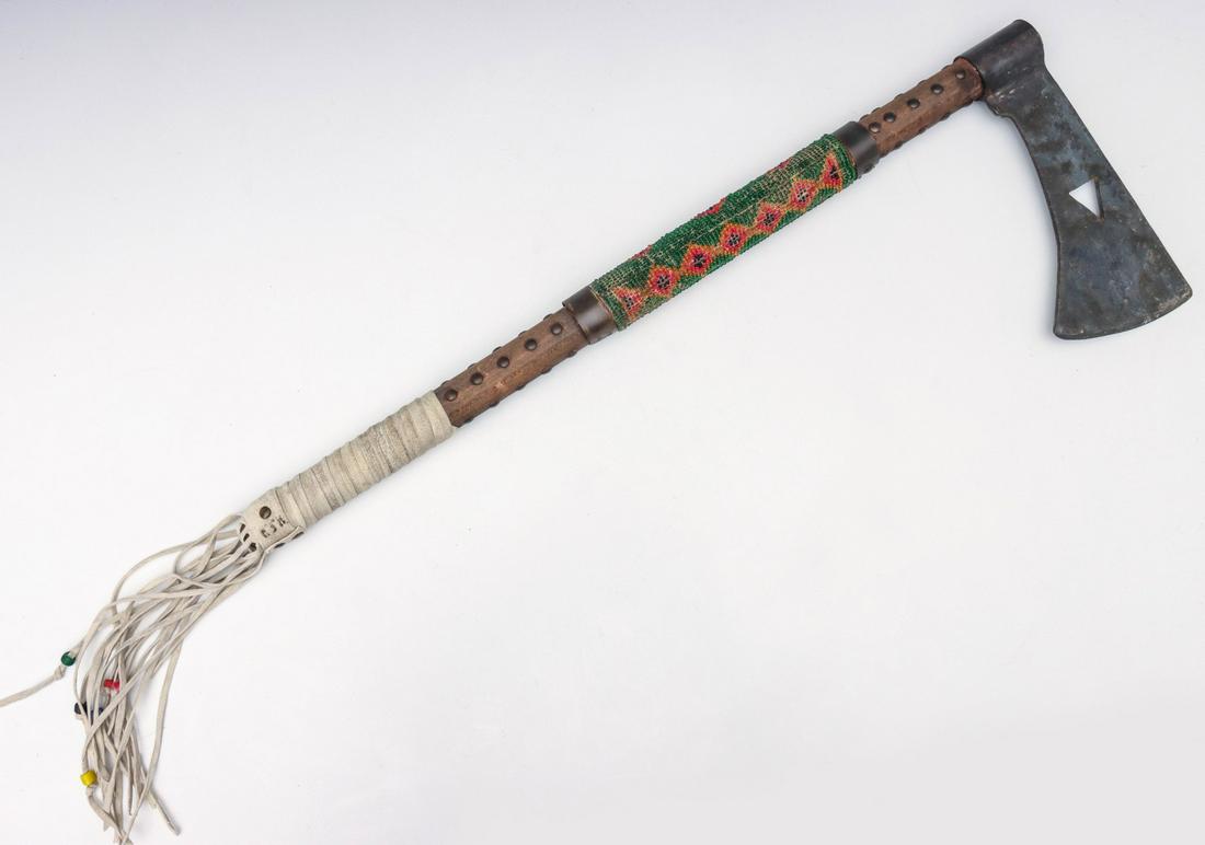 A LATE 20TH CENTURY NATIVE STYLE TOMAHAWK WITH BEADING: The iron head on wood handle with beaded portion, hide fringe and studs. Measures 24 inches long. We happily provide seamless in-house packing and shipping services on nearly everything we sell.
