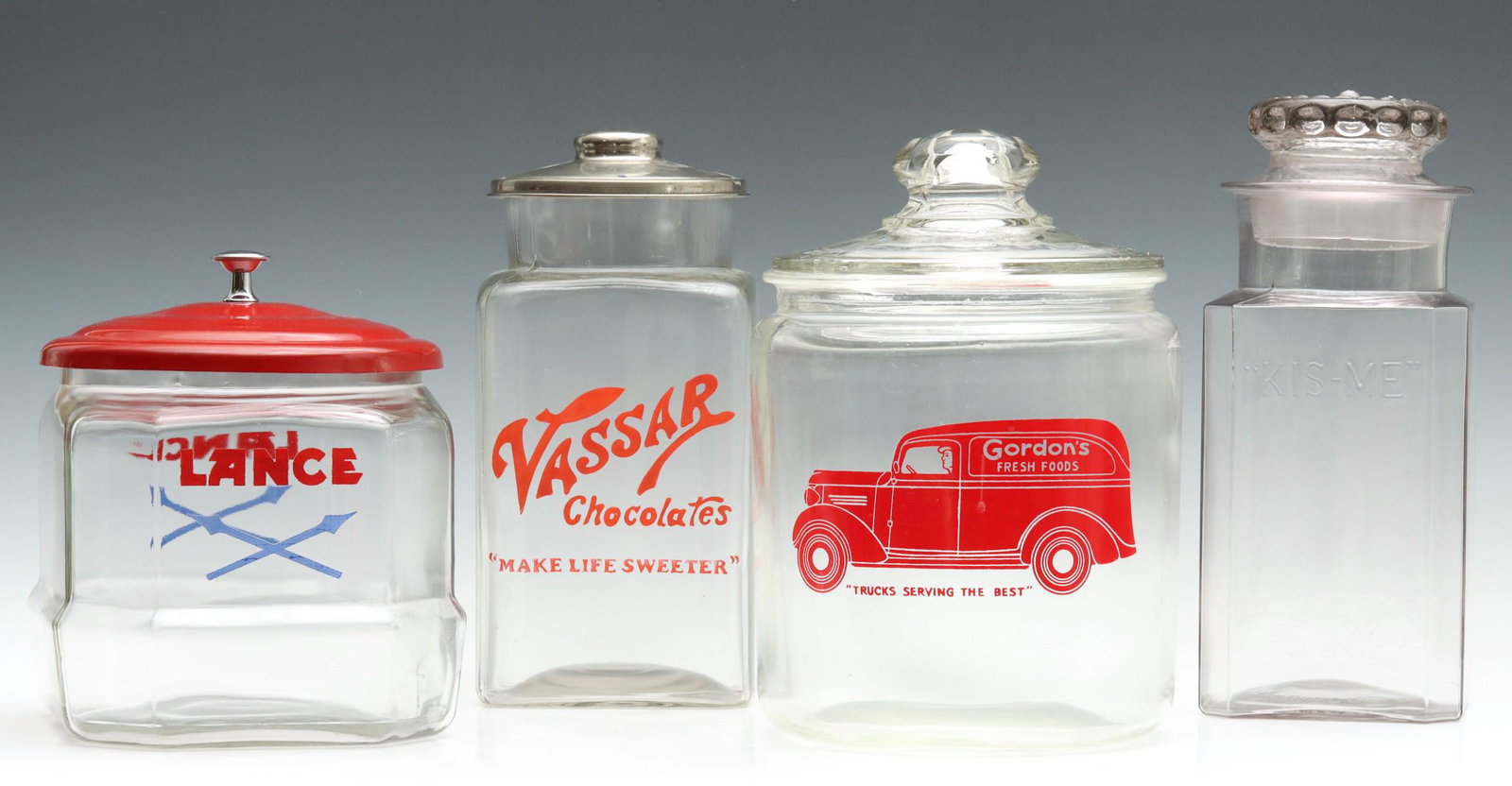 FOUR ADVERTISING CANDY, GUM AND COOKIE JARS CIRCA 1930s: Three painted glass soda fountain and drug store countertop advertising jars for Lance Candy, Vassar Chocolates, Gordon Cookies and a jar with embossed letters of 'KIS-ME Gum.' Sizes range from 8.5 x 