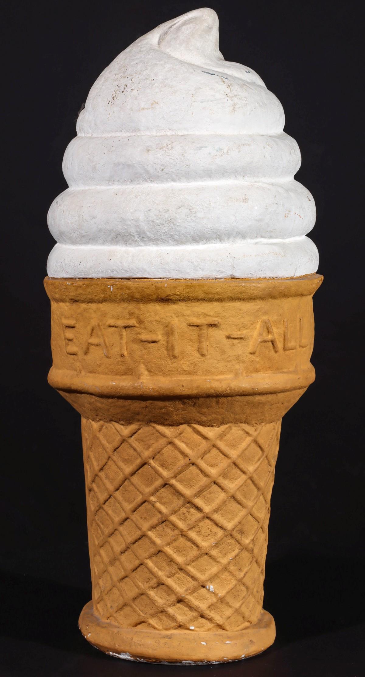 AN EAT-IT-ALL PAPIER MACHE ICE CREAM CONE DISPLAY: The ice cream cone advertising display of papier mache with enamel coating and embossed lettering 'EAT-IT-ALL,' equipped with a coin slot and stopper for a bank. Measures 21 x 8.5 x 8.5 inches. We hap
