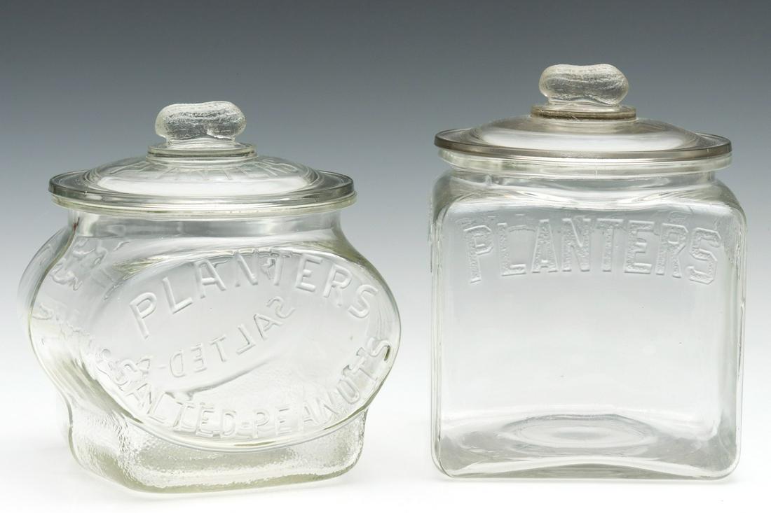 TWO DIFFERENT PLANTER'S PEANUTS ADVERTISING JARS: The drug store countertop jars with embossed lettering and figural peanut lid finial. Measures 8.5 x 7.25 x 7 and 9 x 7 x 7 inches. We happily provide seamless in-house packing and shipping services o