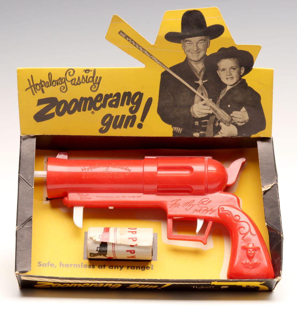 A HOPALONG CASSIDY ZOOMERANG GUN IN ORIGINAL DISPLAY: The red plastic pistol with embossed lettering and images along with Zoomerang roll in original display. Measures 7 x 10.25 x 6 inches. We happily provide seamless in-house packing and shipping servic