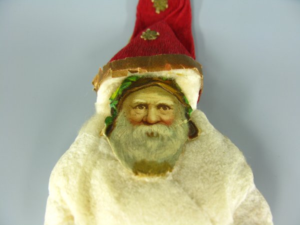 VICTORIAN COTTON SANTA CLAUS CHRISTMAS ORNANMENT: Measures 8 inches, two tiered white cotton coat and trousers, red crepe paper pointy cap, chromolitho face.