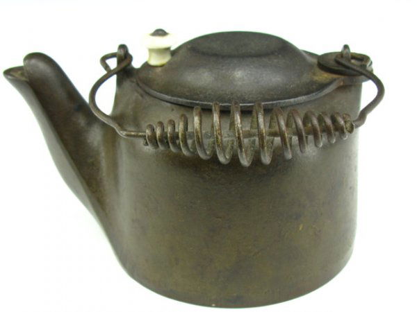 A WAGNER WARE CAST IRON TEA KETTLE: Measures 3.5 x 6.5 inches. Sliding top lid with porcelain knob, wire handle with coil grip. Incised maker mark to bottom.