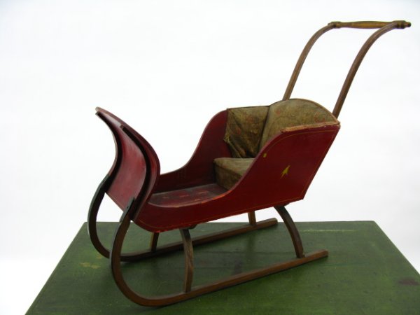 VICTORIAN CHILD'S PUSH SLEIGH IN OLD PAINT: 11.5 x 30 inches, 25 inches up to handle. Old red paint with yellow pinstripes, padded paisley interior. Tacked steel clad runners.