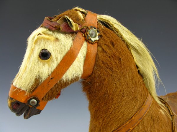 CIRCA-1903 TOY HORSE ON WHEELS: Stands 13.5 inches, 12 inches long. Wood base with metal wheels. Horse retains 90% original fur, leather saddle, bridle broken, metal rivets and leather rosettes. Glass eyes, wood hooves. 'Germany' ta