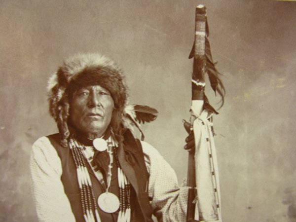 PONCA CHIEF WHITE EAGLE CABINET PHOTO: Excellent albumen image of Chief White Eagle seated in Mistic Studio, Ponca City, OK. Seated in full regalia, holding a peace pipe aloft and wearing an unidentified medallion around his neck. Handwrit
