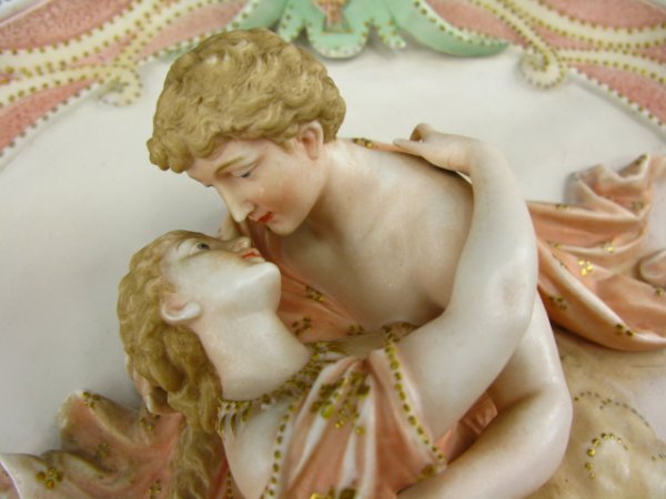 ELABORATE BISQUE PLAQUE CLASSICAL LOVERS: Measures 17 x 14 inches. Classical depiction of a lovers within peach colored robes highlighted with gold enamels. Nice soft pink, gold and aqua-blue tones. Incised 13 to reverse, otherwise unsigned. 