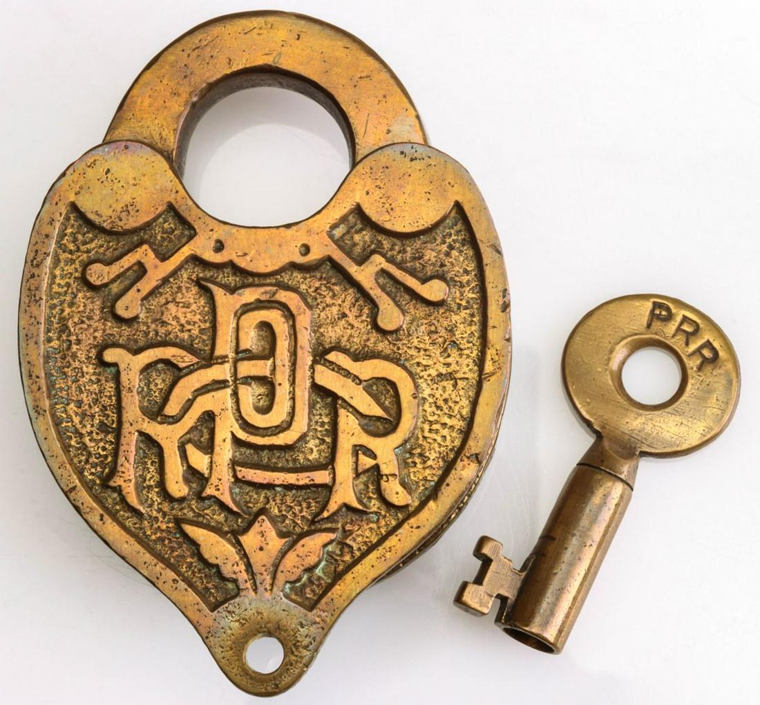 A FANCY CAST BACK PENNSYLVANIA RR PADLOCK WITH KEY: A Slaymaker padlock with fancy raised lettering PRR, stamped Slaymaker on the shackle, tapered barrel key stamped PRR. Measures 3.75 x 2.75 inches. We happily provide seamless in-house packing and shi
