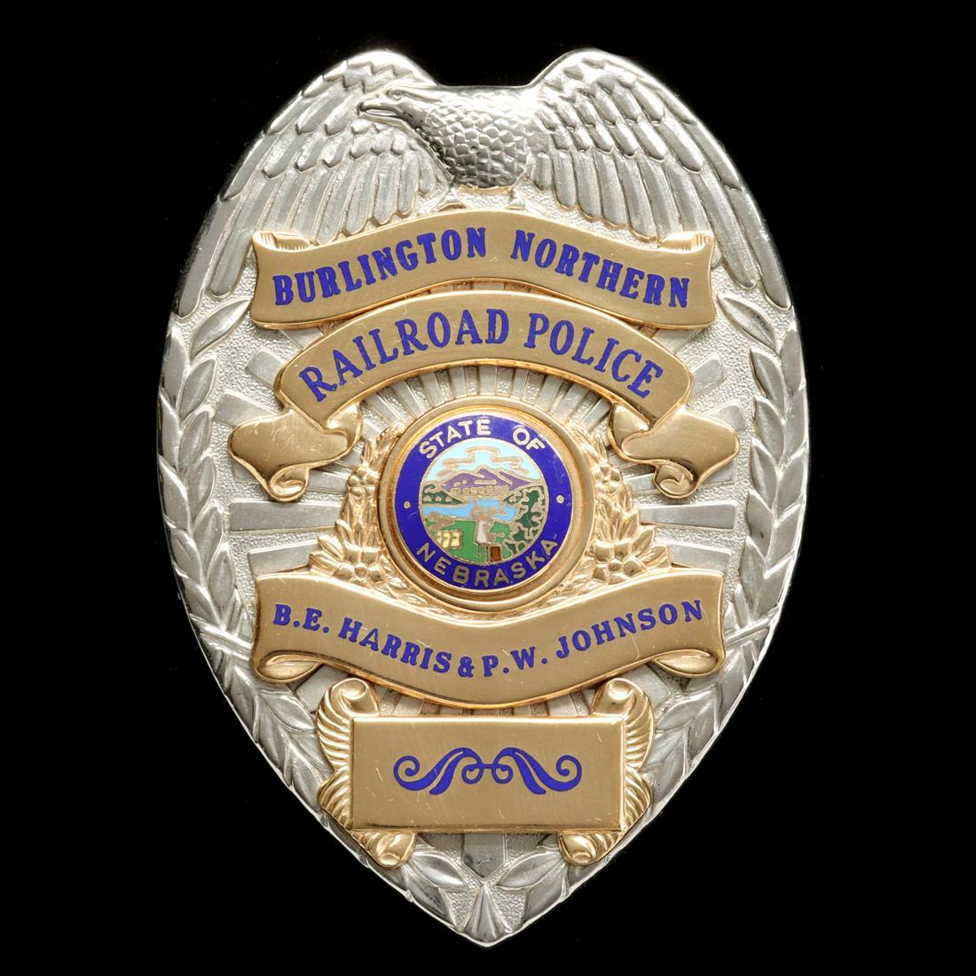 A SHIELD-FORM BURLINGTON NORTHERN RAILROAD POLICE BADGE: The rhodium plated shield with eagle surmount and laurel wreath up each side applied with gold banners that read BURLINGTON NORTHERN RAILROAD POLICE above a central circular seal of the State of Nebra