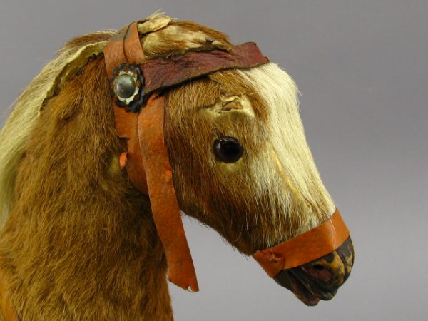 CIRCA-1903 TOY HORSE ON WHEELS: Stands 13.5 inches, 12 inches long. Wood base with metal wheels. Horse retains 90% original fur, leather saddle, bridle broken, metal rivets and leather rosettes. Glass eyes, wood hooves. 'Germany' ta