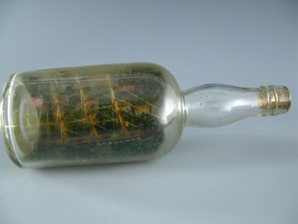 A CLASSIC ANTIQUE SHIP MODEL IN A BOTTLE: Bottle measures 10.25 x 3.5 inches, three mast ship inside with fine detail, background of a village on a hillside, cork stopper firmly in place.