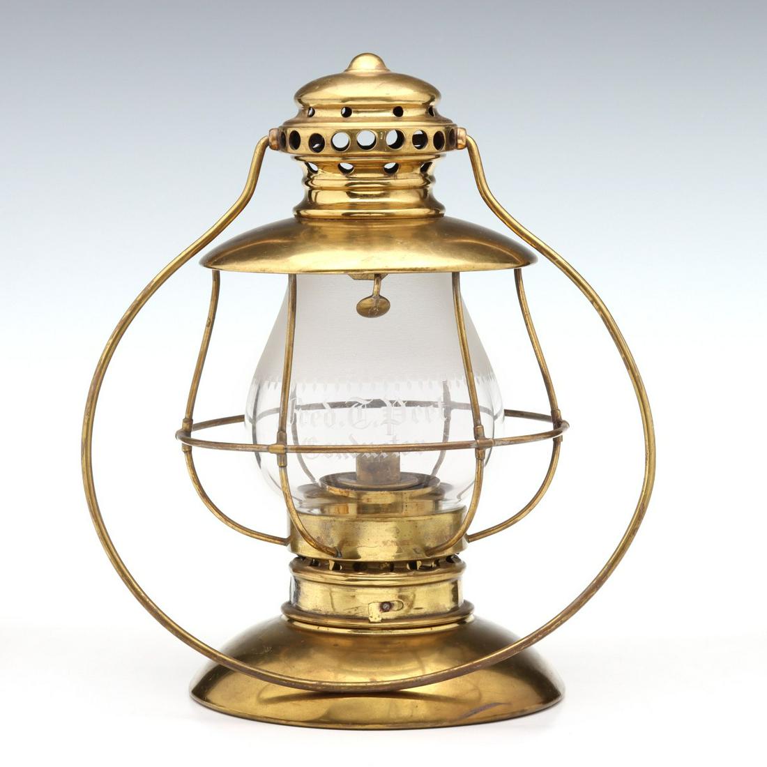 A FINE BRASS PRESENTATION LANTERN WITH ENGRAVED GLOBE: The tiered mushroom cap with vent holes and circular brass bail handle, pronounced visor over wire frame around the removable extended lip globe etched half way down with textured ground ringed in fri