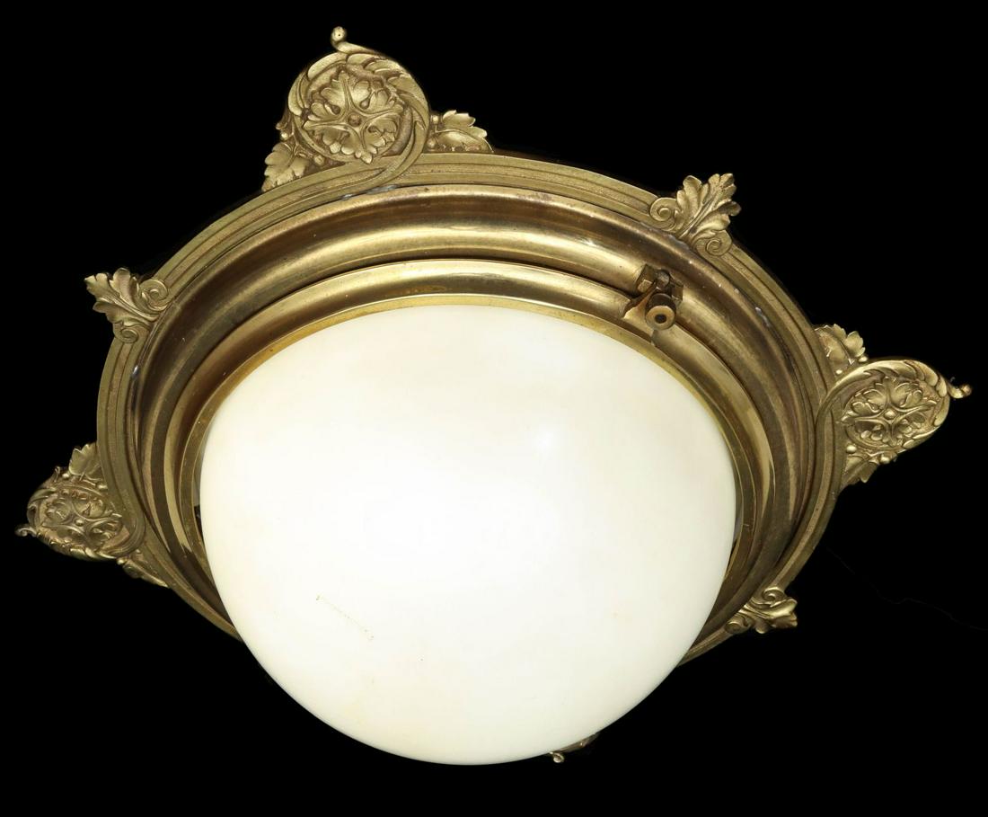 AN ORNATE CAST BRASS AND ART GLASS PULLMAN CAR FIXTURE: The circular flush-mount ceiling fixture with acanthus leaf and scroll castings at four points around the frame interspersed with palmette and scroll decoration, the hinged bezel secures a white ball-