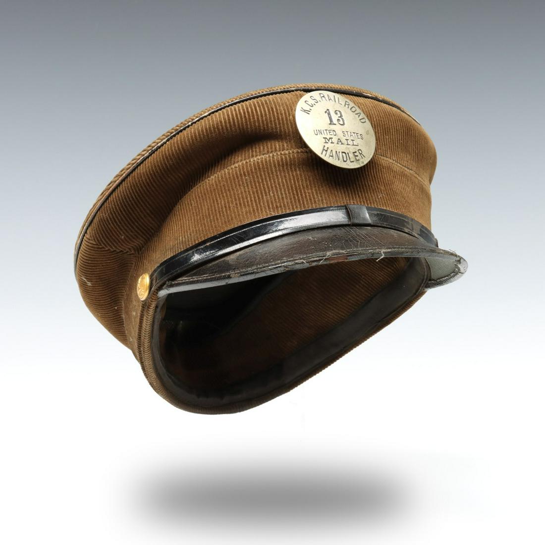 A CORDUROY VISOR CAP WITH KCS MAIL HANDLER BADGE: The unusual corduroy cap with piping, patent leather visor, two brass buttons embossed with the image of a standing mail carrier with outstretched arm holding an envelop in his hand and lettered POD f