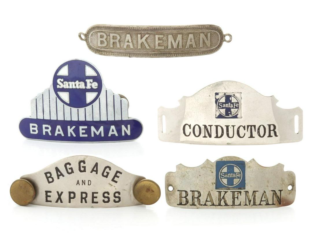 A COLLECTION OF RAILROAD CAP BADGES: The five cap badges include a blue enamel Santa Fe BRAKEMAN badge: Santa Fe BRAKEMAN badge with enameled logo; Santa Fe CONDUCTOR badge with enameled logo; BAGGAGE AND EXPRESS badge signed H.E. Sleepe
