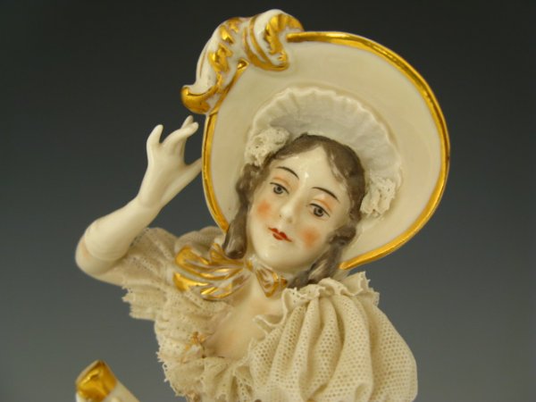 A CONTINENTAL PORCELAIN FIGURE WITH LACE: Nice porcelain figurine of girl with lace dress ornamented with gold painted flowers, bonnet, parasol and slippers, stands 10.5 x 8 inches. Maker marked with crown and underglazed incised 1876.