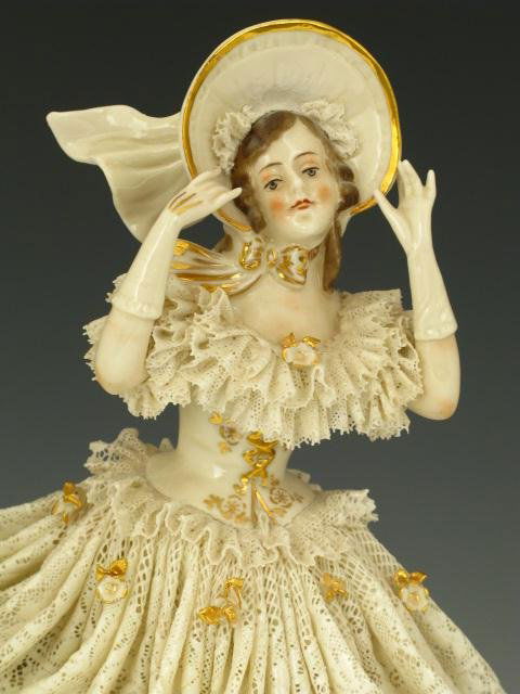 A CONTINENTAL PORCELAIN FIGURE WITH LACE: Nice porcelain figurine of girl with lace dress ornamented with gold painted flowers, bonnet and slippers, stands 10.5 x 8 inches. Maker marked with crown and underglazed incised 1875.