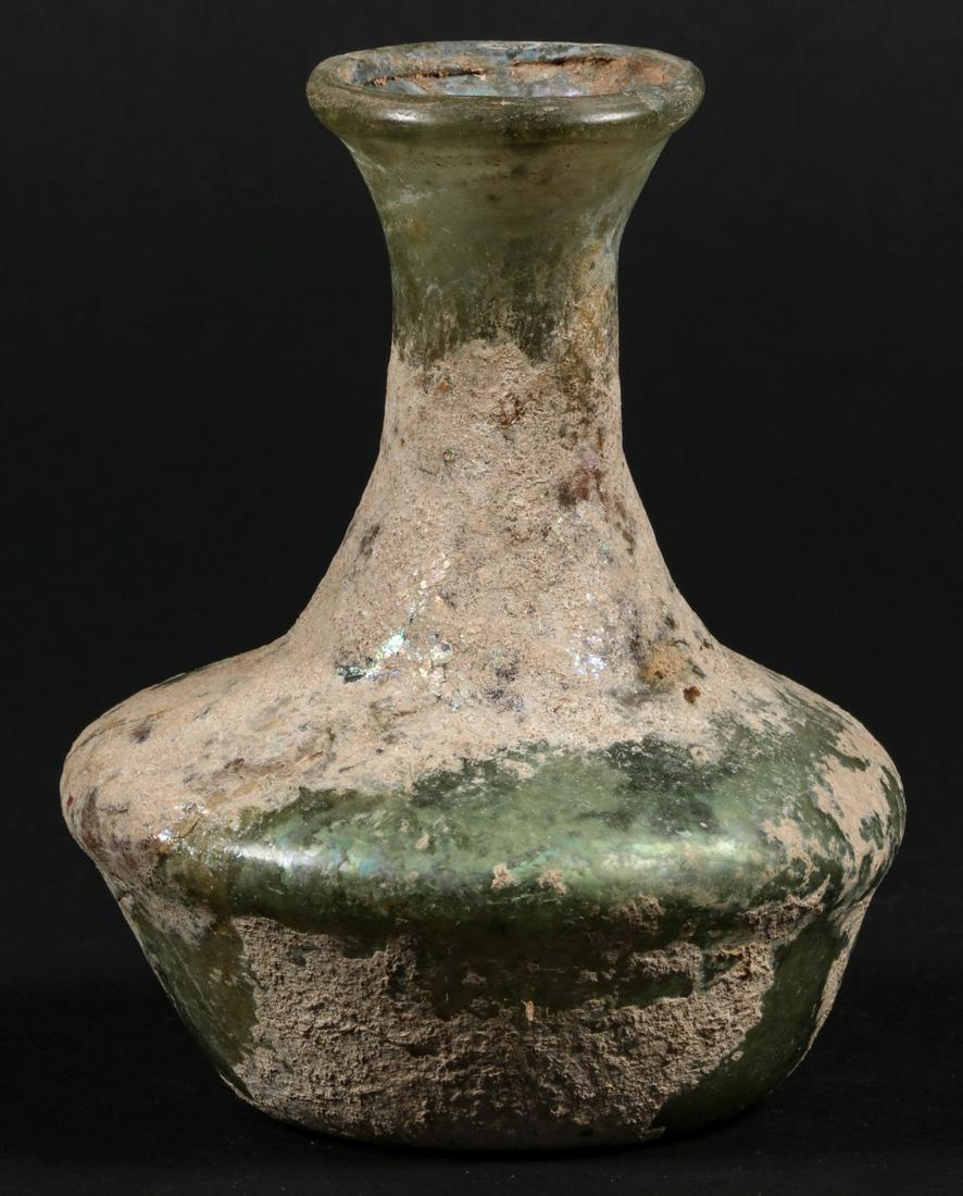A ROMAN GLASS BOTTLE VASE: The globular form with waisted neck in translucent green glass now iridescent and with accretions encrusting the surface. Measures 4 x 3.5 inches. Provenance: The multi-generation collection of an ear