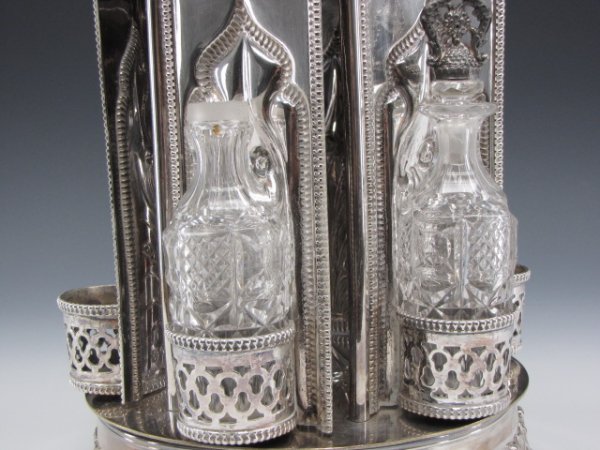 AN 1855 GOTHIC MECHANICAL SILVER CASTOR: A very rare and beautiful silver plated dinner castor that, with a twist of the grape motif handle, mechanically swings open the six doors with gothic arches that would hold the cut glass bottles in s