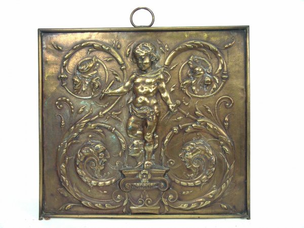 A BRASS CHERUB MOTIF FIRE SCREEN IN HIGH RELIEF: Formerly a floor standing piece with decoration of a full length cherub atop a Classical theme capitol and flanked by rococo swirls all in very high relief. A great decorative element, this measures 2